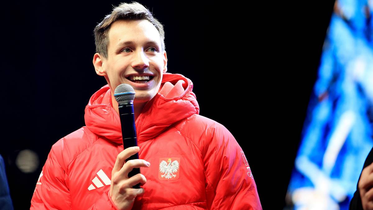 Kacper Tomasiak w kurtce z godłem Polski, trzymający mikrofon i uśmiechający się.