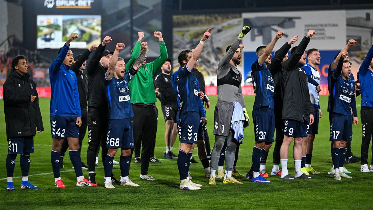 Piłkarze Motoru Lublin świętują zwycięstwo na boisku, podnosząc ręce w geście triumfu.