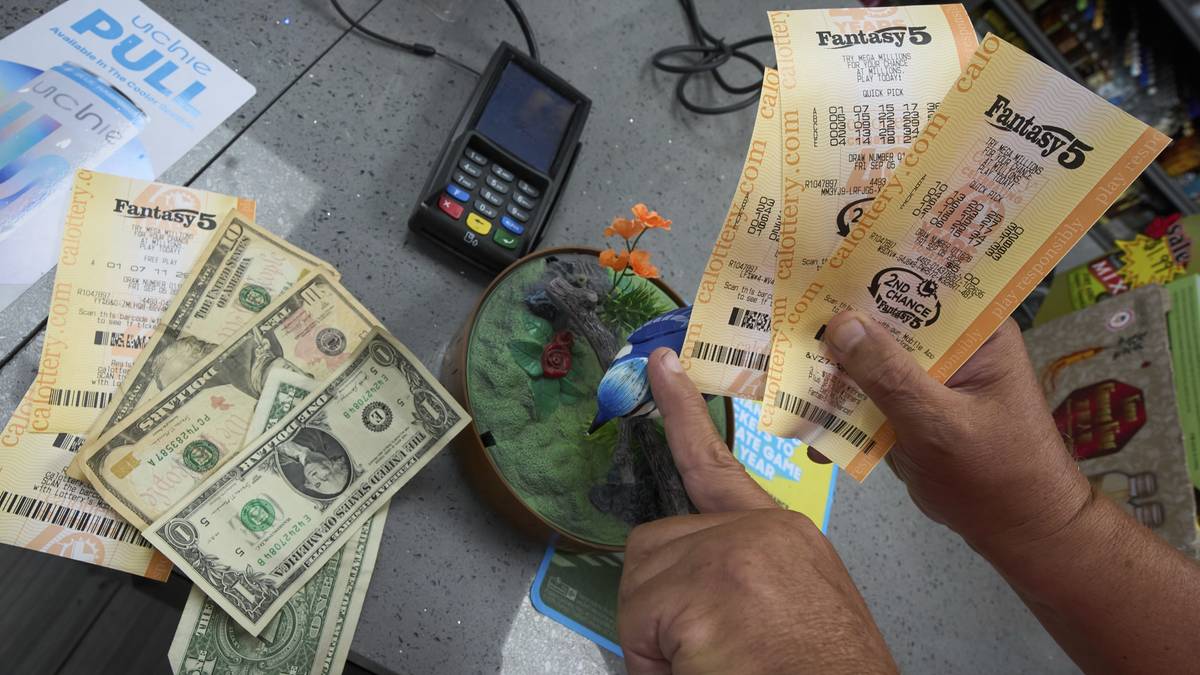 Dłoń trzyma kilka kupon&oacute;w loterii "Lucky 5" i banknoty dolarowe.