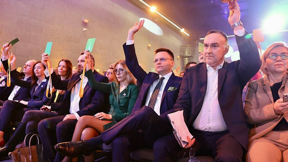 Ludzie siedzący w rzędach, niekt&oacute;rzy z podniesionymi rękami.