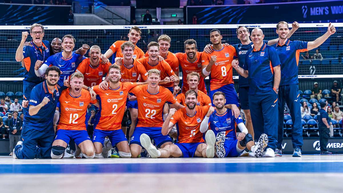 Dwuwarstwowa grupa siatkarzy w pomarańczowych strojach pozuje do zdjęcia, w pierwszej warstwie klęczą, w drugiej stoją, wszyscy uśmiechają się.