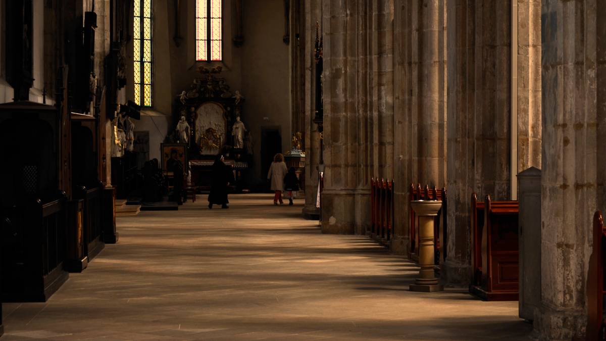 Wnętrze kościoła z rzędem drewnianych ławek po prawej stronie i kolumnami po lewej. W głębi widoczne są okna witrażowe i ołtarz.