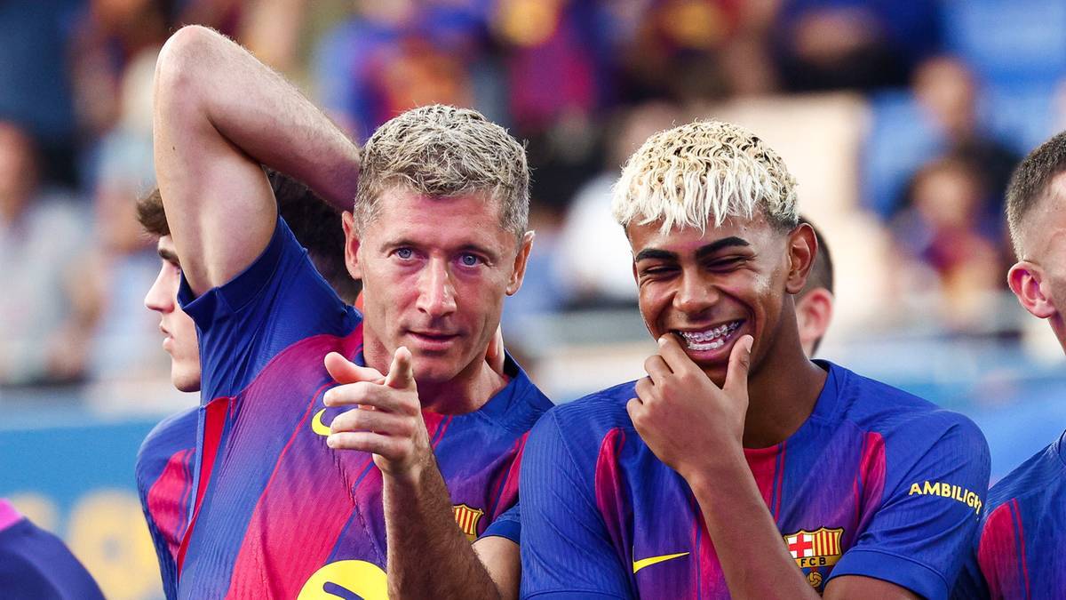 Dwóch piłkarzy FC Barcelony w niebiesko-czerwonych strojach. Po lewej Robert Lewandowski z uniesioną ręką, wskazujący palcem w kierunku widza. Po prawej młody piłkarz z blond włosami uśmiecha się do kamery.