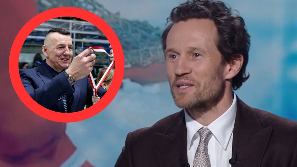 Zdjęcie przedstawia dwie osoby. Po prawej stronie w zbliżeniu widać mężczyznę mówiącego do kamery, ubranego w garnitur i białą koszulę z krawatem. Po lewej stronie, w czerwonym okręgu, widoczny jest inny mężczyzna w granatowym garniturze, który pokazuje medal z biało-czerwono-białą wstążką.