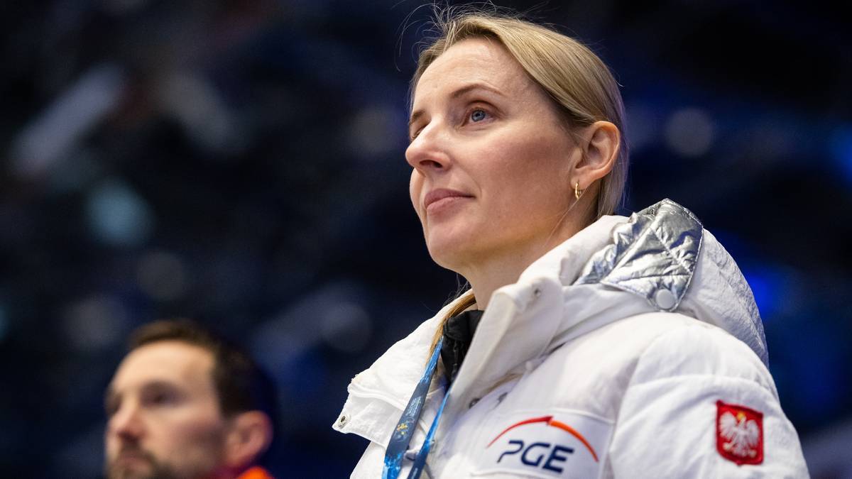 Portret kobiety w białej kurtce sportowej z emblematem Polski i logo PGE, patrzącej w bok z uwagą.