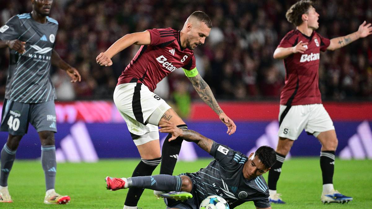 Piłkarze walczą o piłkę na boisku, jeden z nich leży na ziemi.