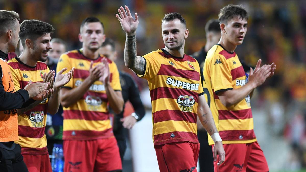 Piłkarze w ż&oacute;łto-czerwonych strojach wychodzą na boisko.