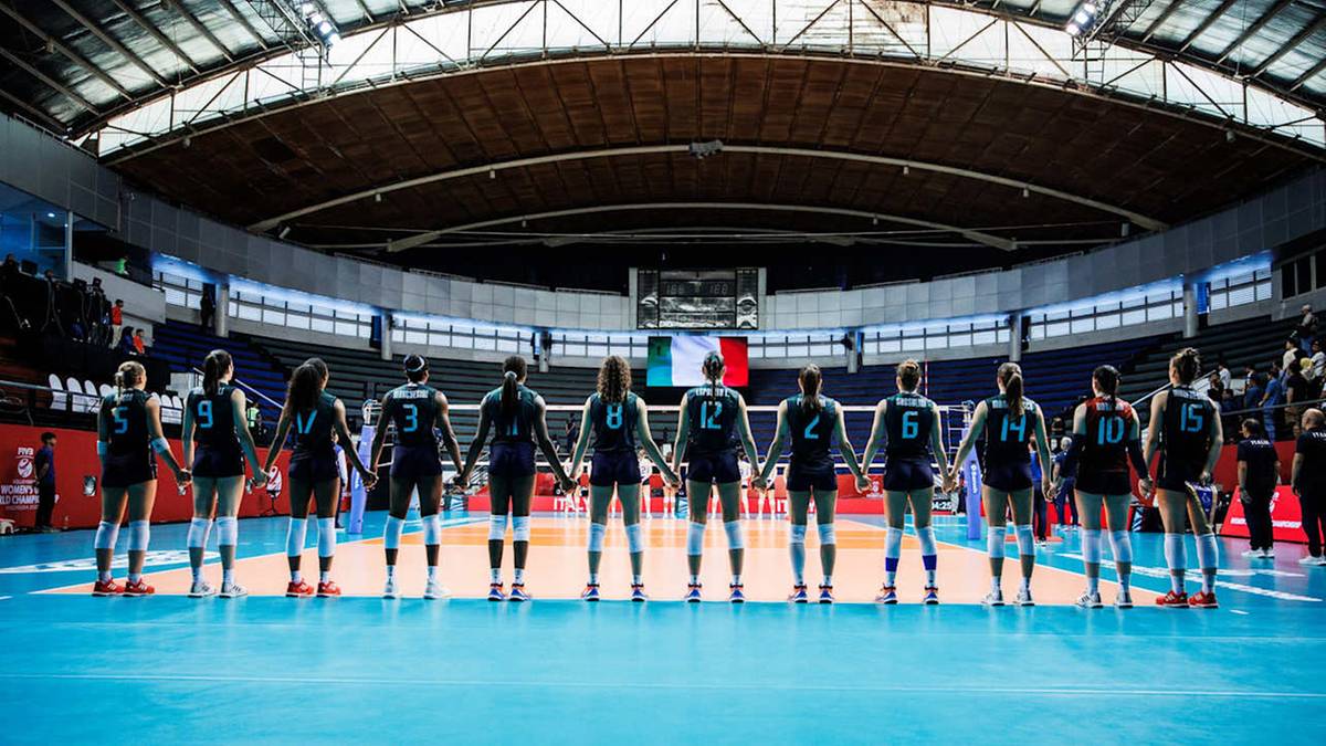 Drużyna siatkarska ustawiona na środku boiska, tyłem do widza, przygotowana do meczu.