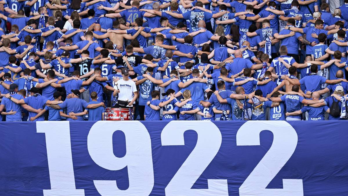 Tłum kibic&oacute;w w niebieskich koszulkach stojących za transparentem z napisem "1922".