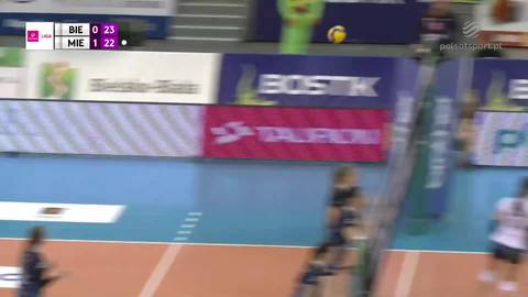 Fragment meczu siatk&oacute;wki z widoczną siatką, boiskiem i tablicą wynik&oacute;w.