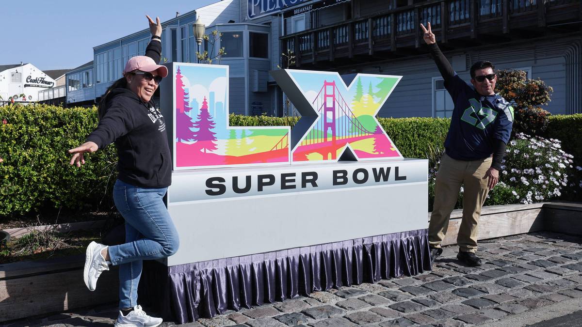 Dwie osoby pozują radośnie przy wielkim napisie "LX SUPER BOWL" na tle budynku z napisem "PIER 39".