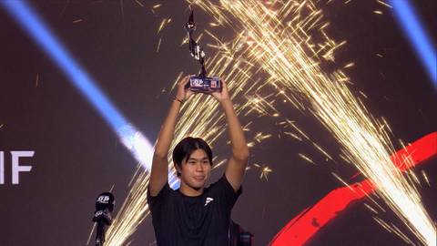 Młody mężczyzna trzymający puchar nad głową na tle fajerwerk&oacute;w.