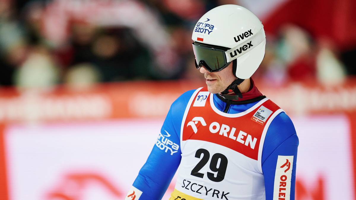 Skoczek narciarski w białym kasku i goglach narciarskich, z numerem 29 na piersi.