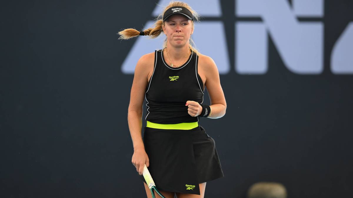 Magdalena Fręch podczas meczu tenisowego, w czarnym stroju sportowym z żółtymi akcentami, trzymająca rakietę tenisową.