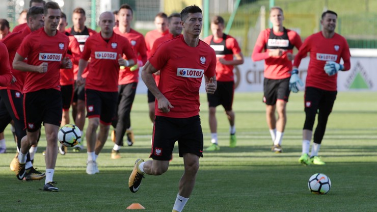 Robert Lewandowski na pierwszym planie, biegnie podczas treningu reprezentacji Polski. W tle widoczni inni piłkarze w czerwonych koszulkach.