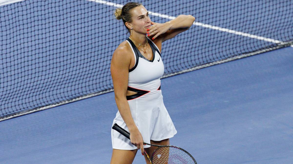 Aryna Sabalenka, tenisistka, w białym stroju, z rakietą w ręku, na korcie tenisowym, z siatką w tle.