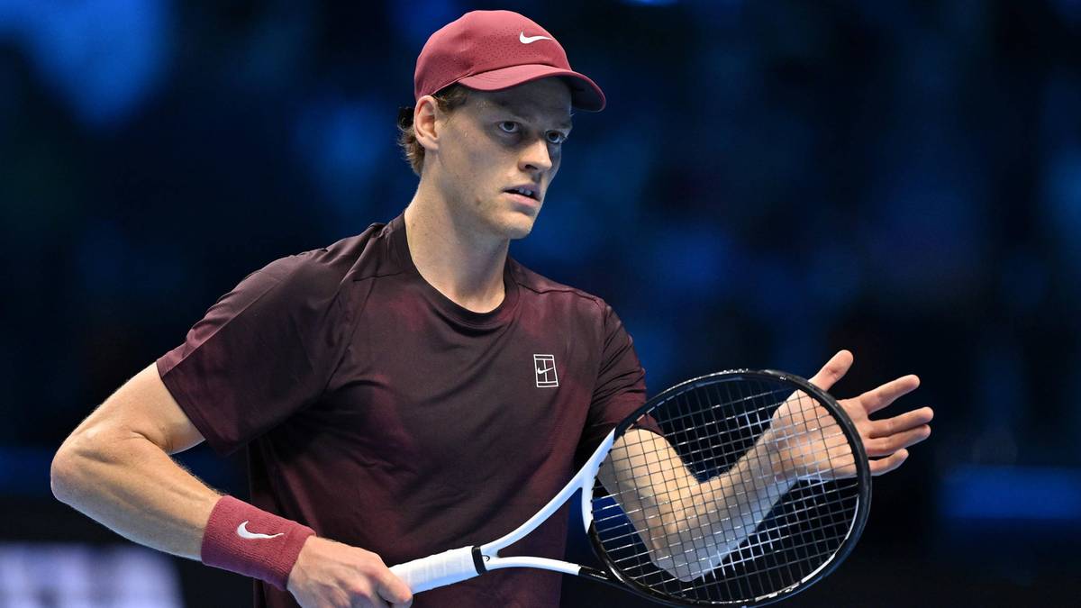 Tenisista Jannik Sinner w bordowym stroju sportowym i czerwonej czapce, trzymający rakietę tenisową.