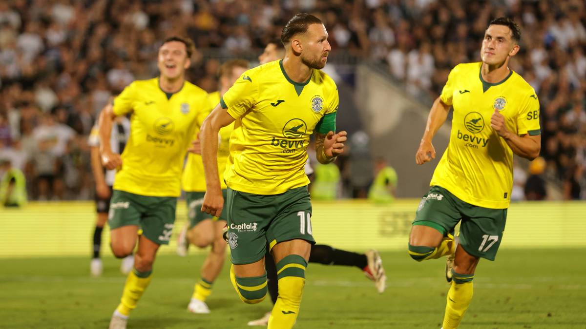 Piłkarze w żółtych koszulkach i zielonych spodenkach biegną po boisku piłkarskim.