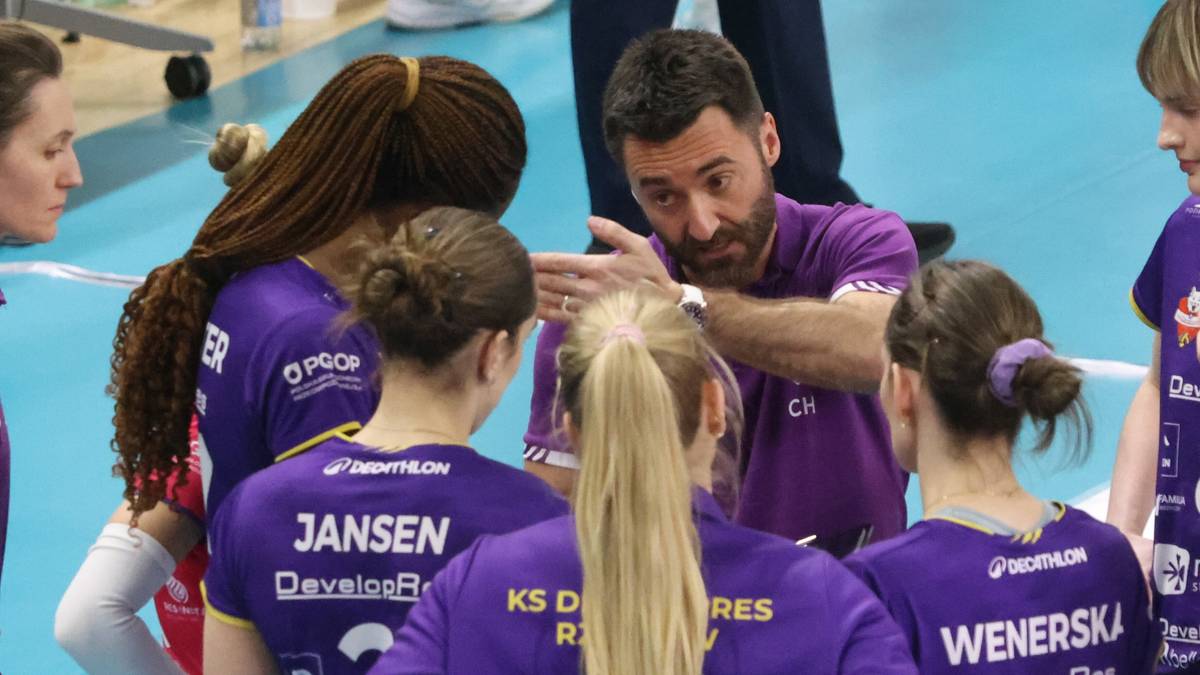 Trener siatkarki w fioletowych strojach sportowych udziela wskaz&oacute;wek podczas przerwy w meczu.