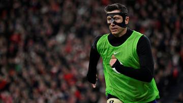 Piłkarz Robert Lewandowski w zielonej kamizelce treningowej i masce na twarzy biegnie na boisku.