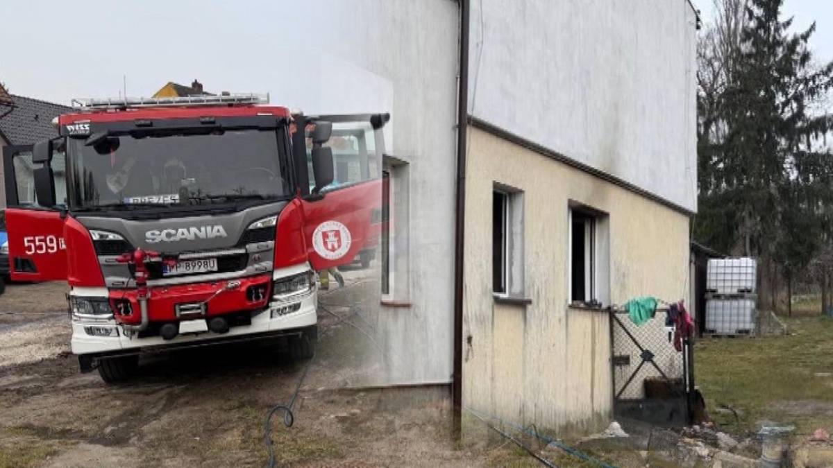 W&oacute;z strażacki stoi obok budynku mieszkalnego z widocznymi śladami pożaru na fasadzie i w oknach.