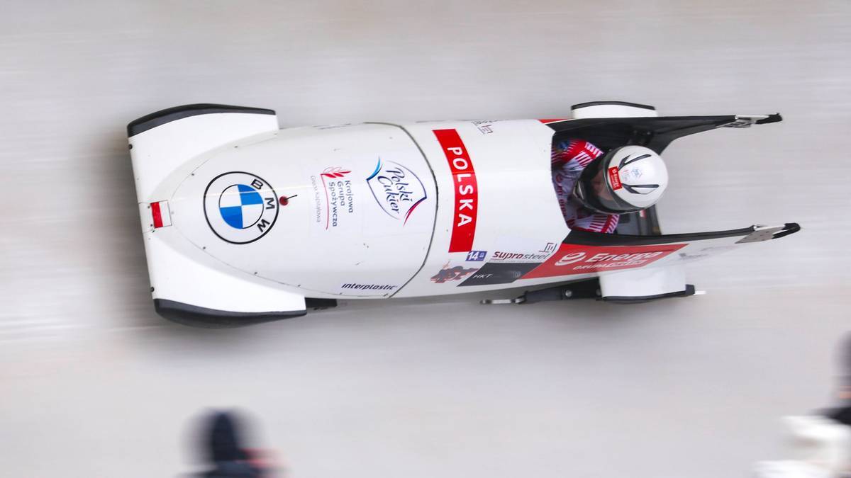 Dwójka bobslejowa z polską flagą podczas zawodów, z widoczną zawodniczką w kasku.