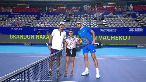 Dw&oacute;ch mężczyzn i jedna kobieta stoją na korcie tenisowym, trzymając rakiety tenisowe. W tle widać trybuny z widzami.