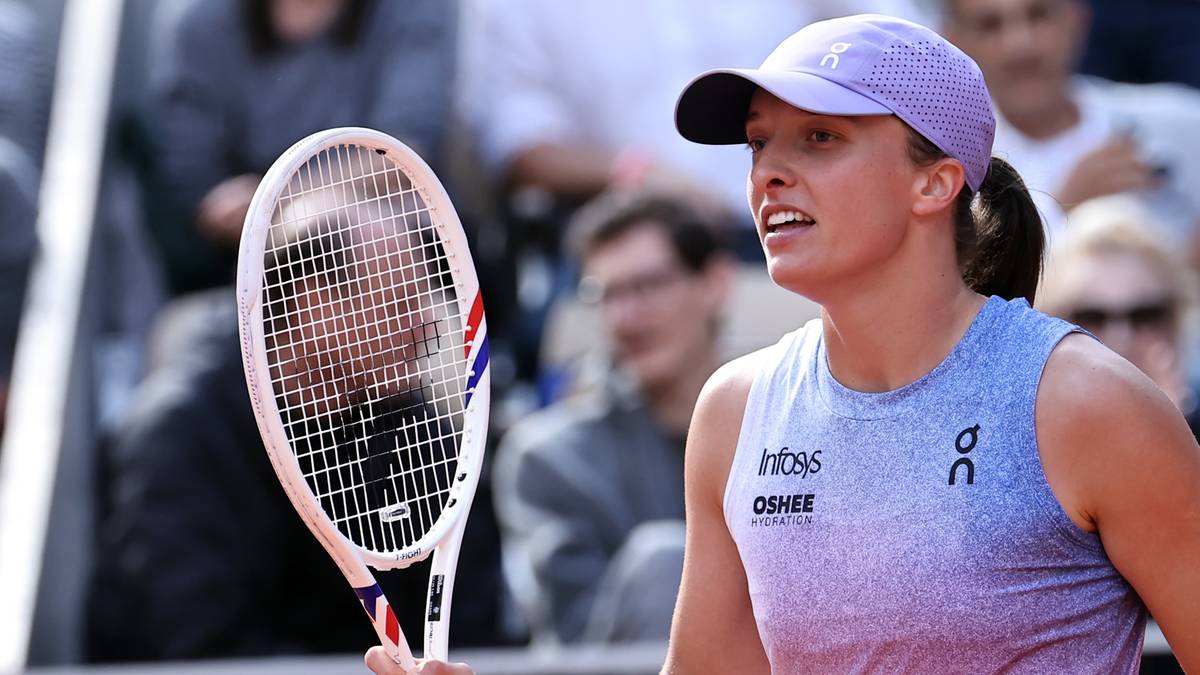 Iga Świątek z rakietą tenisową w ręku, ubrana w sportowy strój z czapką na głowie, na tle publiczności.