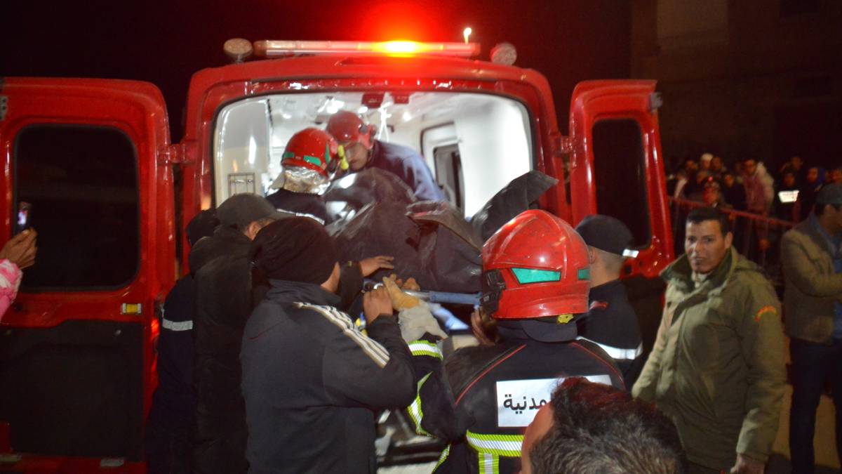 Ratownicy w kaskach wyciągają osobę na noszach z karetki pogotowia nocą.