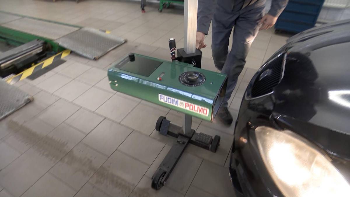 Pracownik stacji diagnostycznej wykonuje badanie techniczne pojazdu, używając urządzenia do pomiaru świateł.