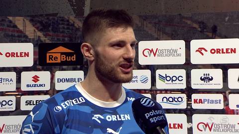 Mężczyzna udzielający wywiadu na tle paneli sponsorskich.