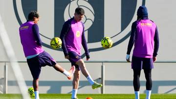 Trzech piłkarzy w różowych strojach treningowych ćwiczy z piłkami na boisku.