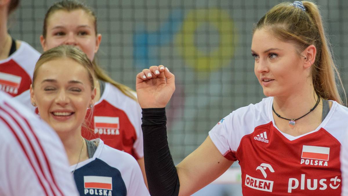 Dw&oacute;ch młodych siatkarek w białych koszulkach z napisem "POLSKA" i logo "ORLEN PLUS". Jedna z nich, z prawej, uśmiecha się do przodu, druga, z lewej, patrzy w d&oacute;ł z uśmiechem.