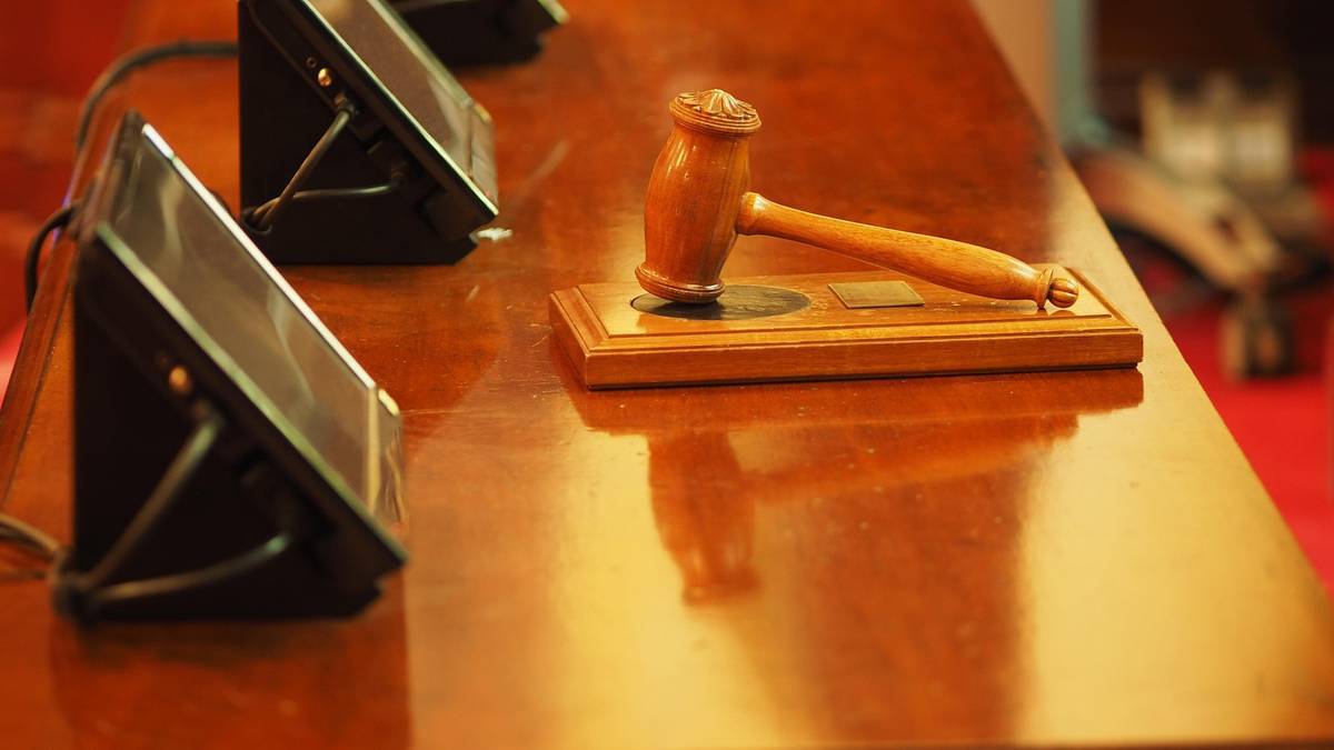 Młotek sędziowski położony na drewnianej podstawie na stole w sali sądowej.