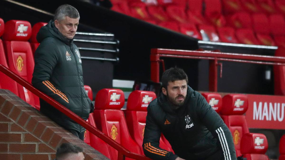 Dwóch trenerów Manchesteru United w dresach siedzi na trybunach stadionu.