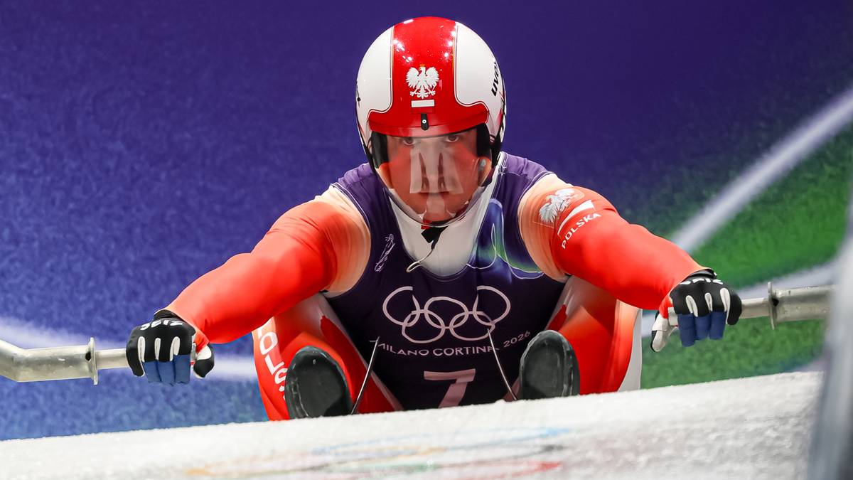 Zawodnik sport&oacute;w zimowych w kasku i kombinezonie jedzie na sankach.