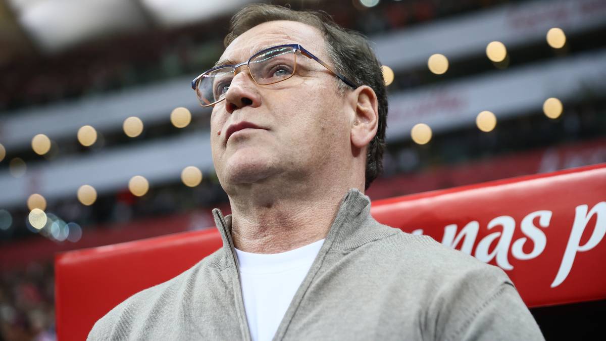 Mężczyzna w okularach i szarej bluze patrzy w g&oacute;rę na stadionie.