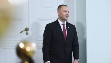 Mężczyzna w garniturze i krawacie idzie w kierunku białych drzwi.