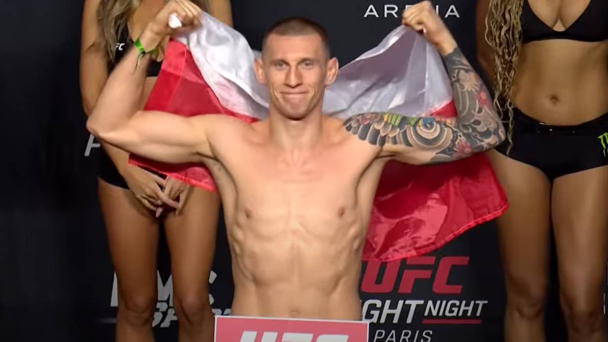 Polski zawodnik MMA Robert Ruchała z polską flagą, stojący między dwiema kobietami.