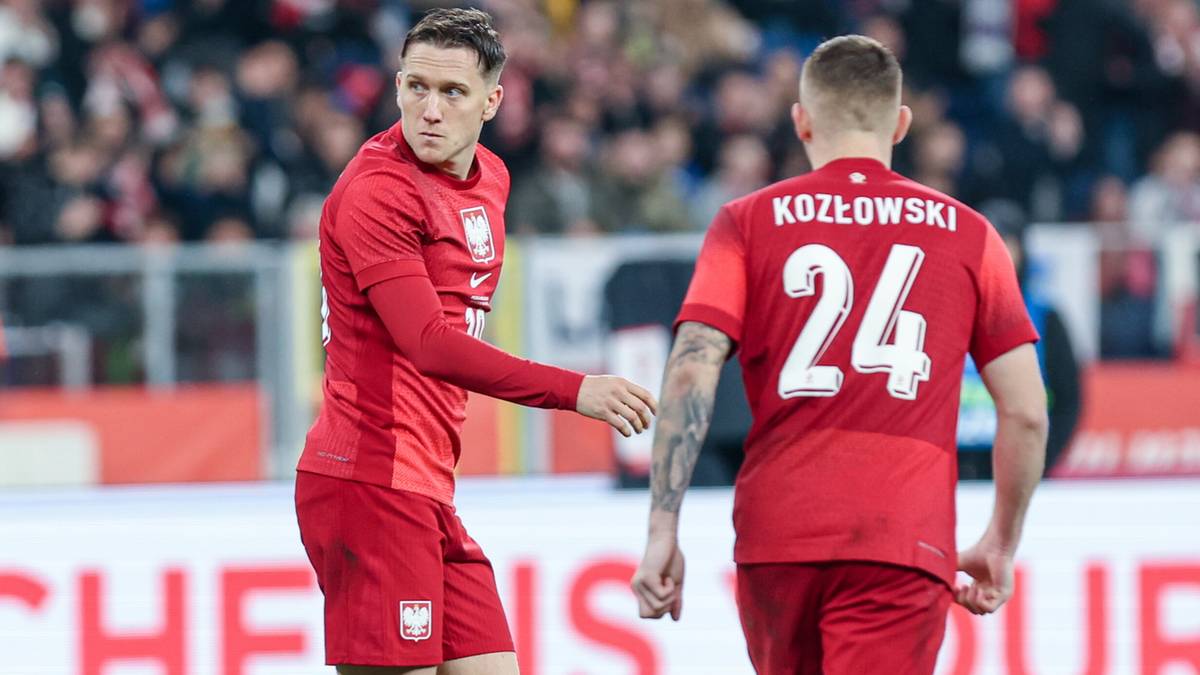 Dwóch piłkarzy reprezentacji Polski w czerwonych strojach na tle trybun.