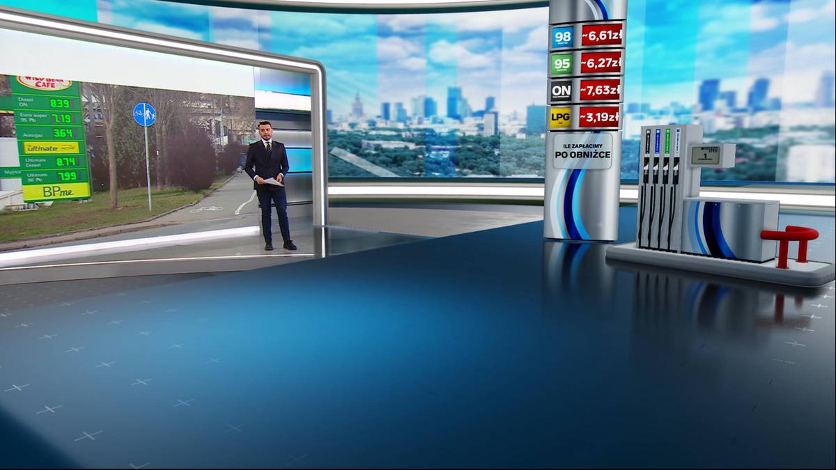 Dziennikarz w garniturze prezentuje informacje o cenach paliw na ekranie. W tle widoczna jest stacja paliw i panorama miasta.