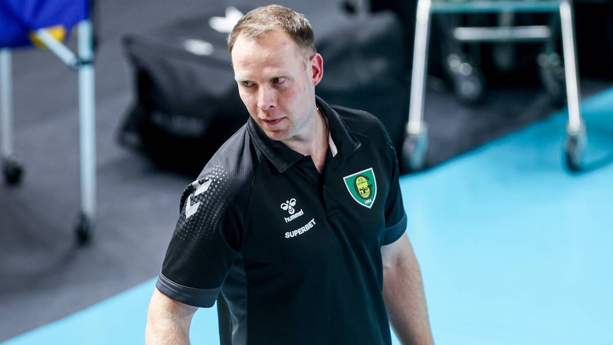 Mężczyzna w czarnej koszulce polo z herbem drużyny sportowej, patrzący w bok z wyrazem koncentracji.