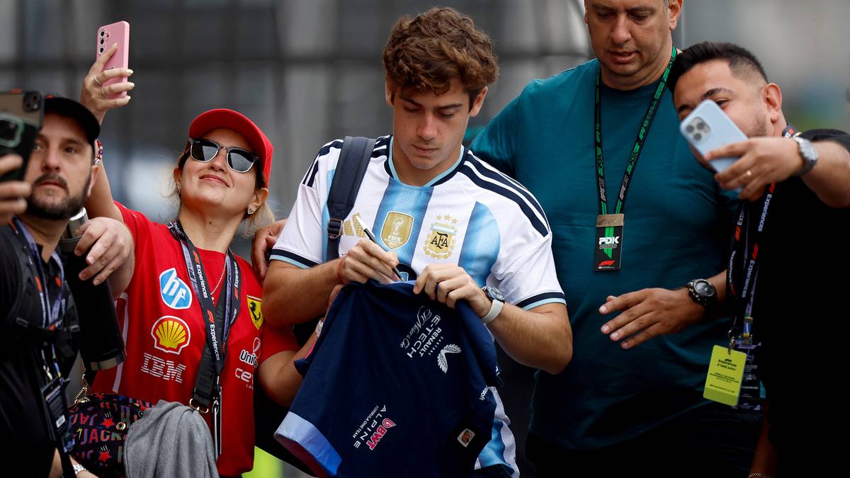 Młody mężczyzna w koszulce reprezentacji Argentyny podpisuje koszulkę piłkarską, otoczony przez fan&oacute;w z aparatami.