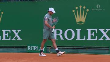 Hubert Hurkacz w stroju tenisowym, w białej czapce, trzyma rakietę i idzie po korcie tenisowym.