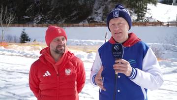 Marcin Bachleda, ubrany w czerwoną kurtkę i czapkę, stoi obok mężczyzny w niebiesko-białej kurtce i granatowej czapce, kt&oacute;ry trzyma mikrofon. Obaj mężczyźni stoją na zewnątrz, w śnieżnym otoczeniu, z drzewami w tle.