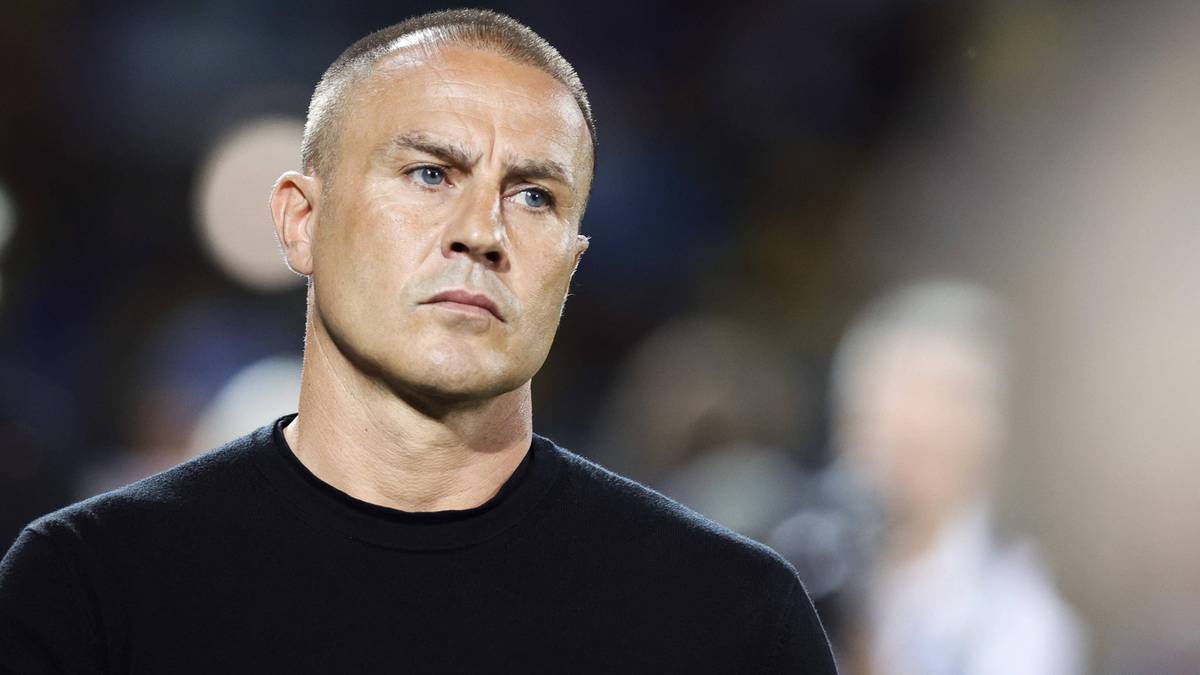 Portret mężczyzny z krótkimi, siwymi włosami, patrzącego z powagą w bok. Nosi czarną koszulkę.