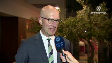 Mężczyzna w okularach i garniturze trzymający mikrofon Polsat Sport, udzielający wywiadu.