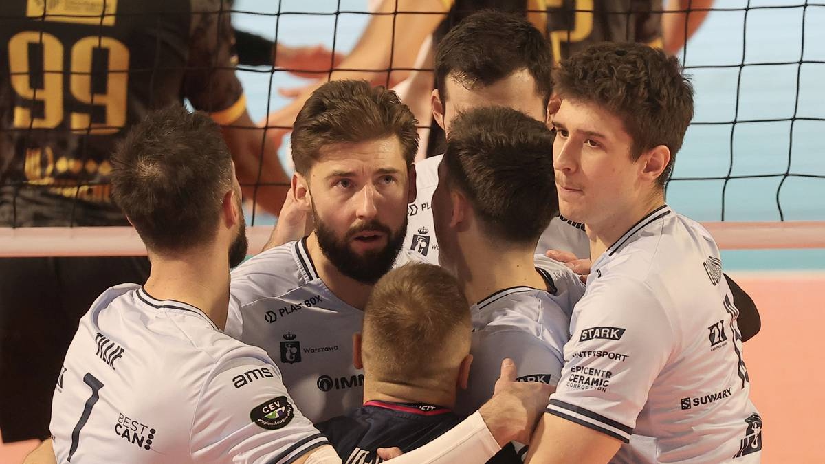Siatkarze w białych koszulkach zbliżeni do siebie, koncentrujący się przed meczem lub po ważnej akcji.