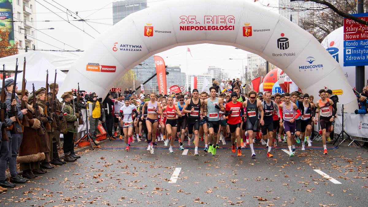 Tłum biegaczy startuje w Biegu Niepodległości pod biało-czerwoną bramą z napisem "Bieg Niepodległości".