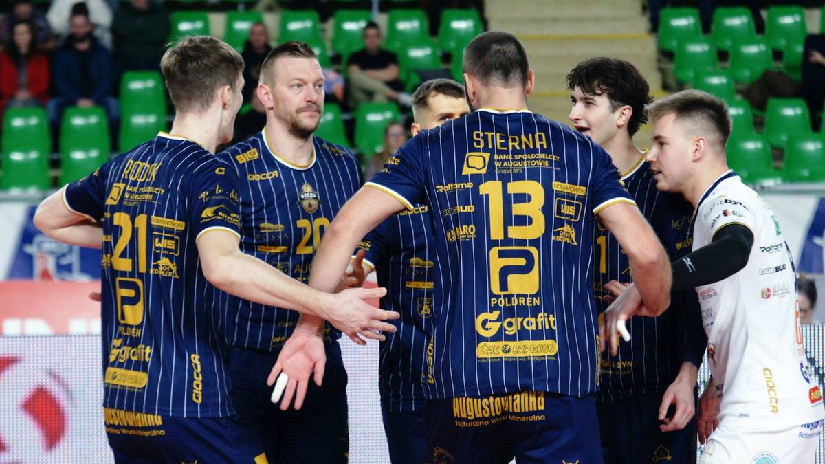 Siatkarze w granatowo-ż&oacute;łtych strojach dyskutują na boisku siatkarskim.